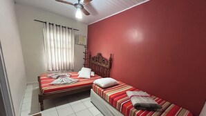 A small, clean room with two beds, a ceiling fan, and a window with curtains. - Pousada Orquidário (Santos)