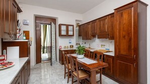 A kitchen with wooden cabinets, a dining table with chairs, and a potted plant. - Grotta di Rita (Turin)