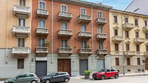 A row of multi-story buildings with balconies, a street, and parked cars. - Grotta di Rita (Turin)