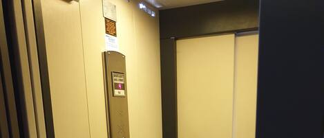 An elevator interior with a control panel, a door, and a carpeted floor.
