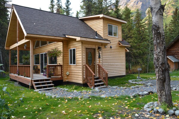 A log cabin with a porch, a deck, and a stone pathway. - Lower Paradise Log Cabin in Moose Pass (Moose Pass)