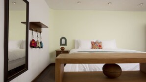 Quarto com estrutura de cama de madeira, mesa de cabeceira com espelho e cabideiro fixado na parede com bolsas.