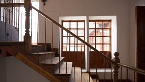 Uma escadaria de madeira com guarda-corpo de metal que leva a uma porta com painéis de vidro.