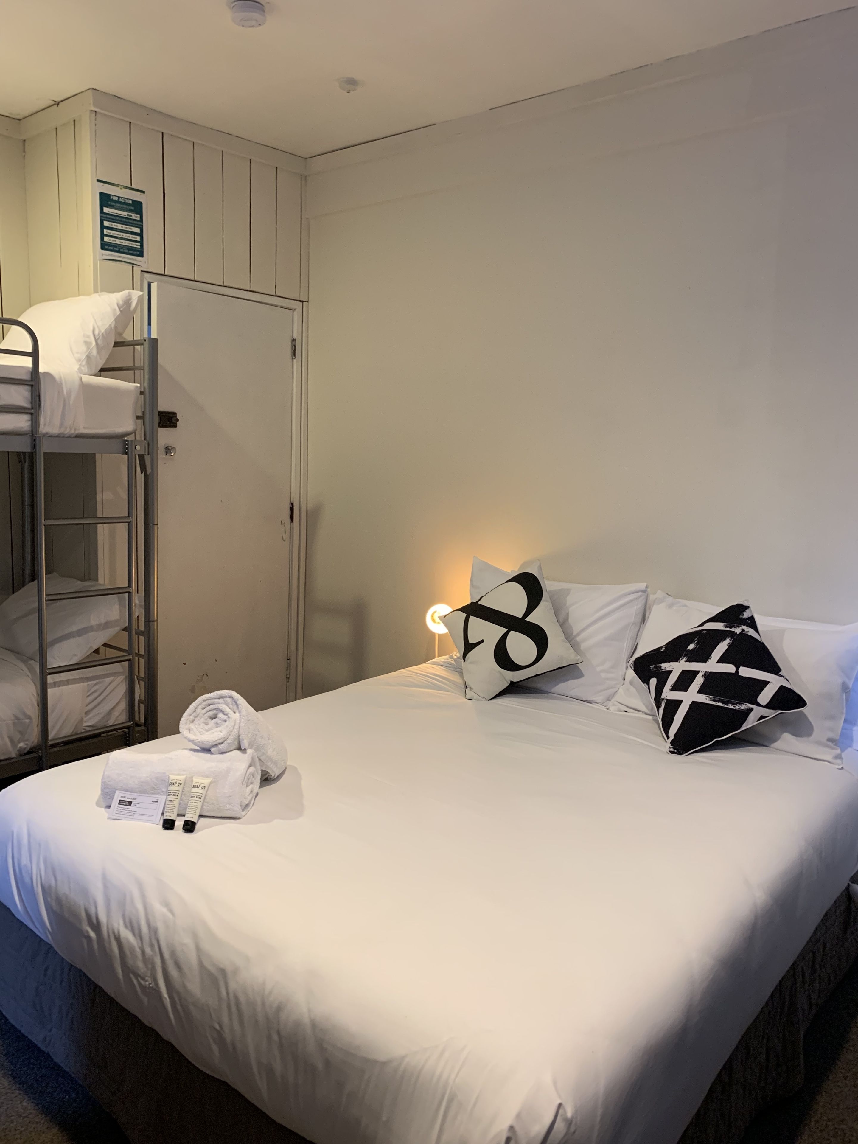 Habitación con literas, una cama individual, una mesita de noche y un estante en la pared.
