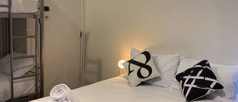 Habitación con literas, una cama individual, una mesita de noche y un estante en la pared.