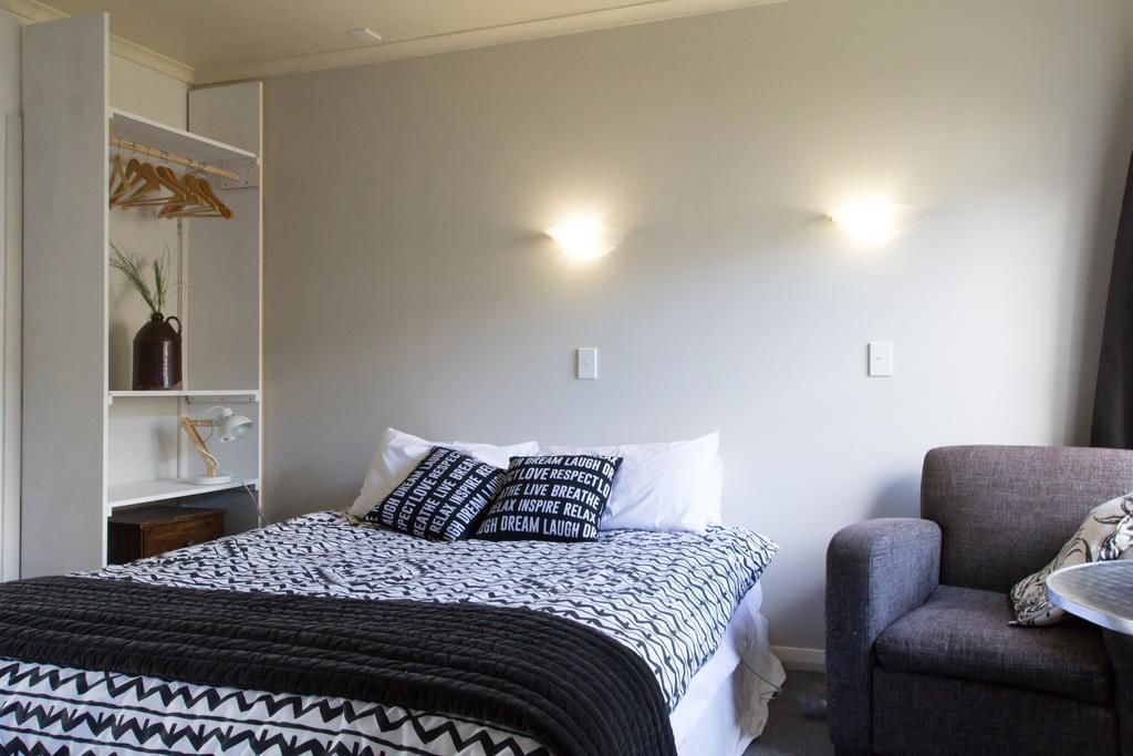 A bedroom with a bed, a chair, a wardrobe, and a wall-mounted light fixture.