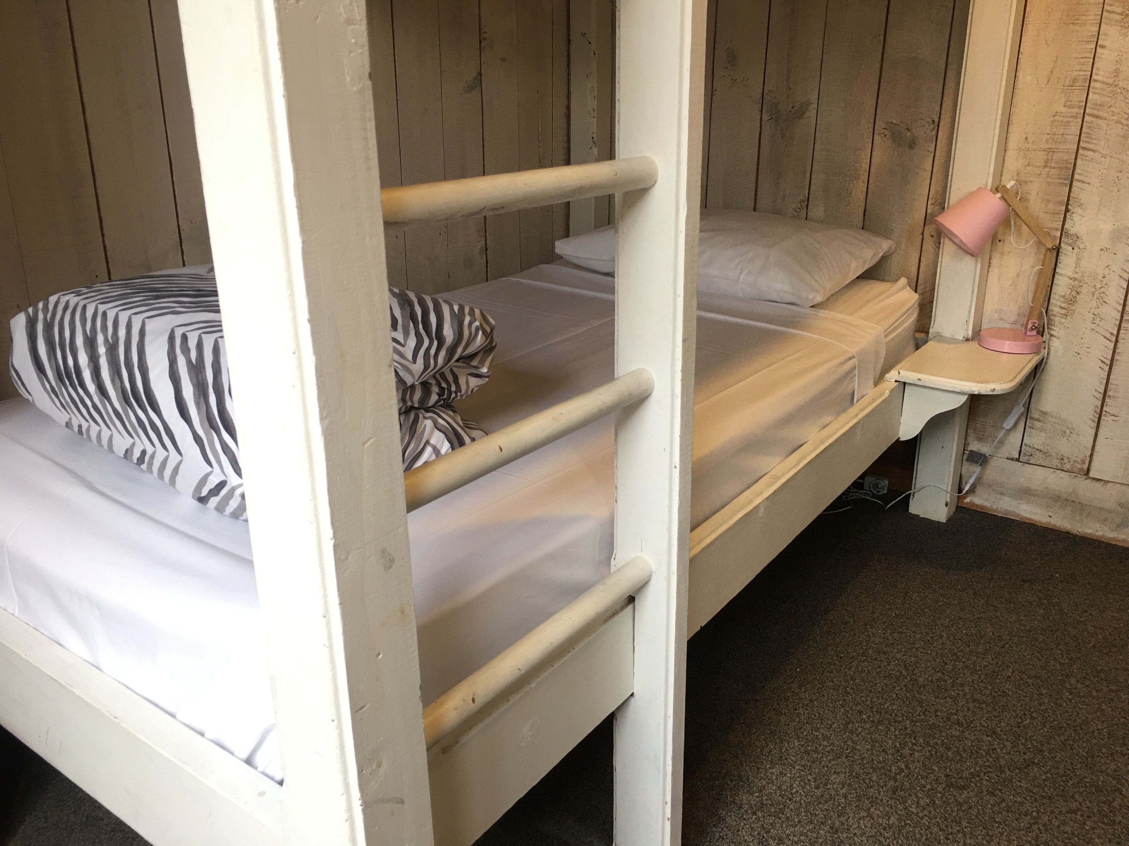 Una cama litera con un almohadón y una manta a rayas.