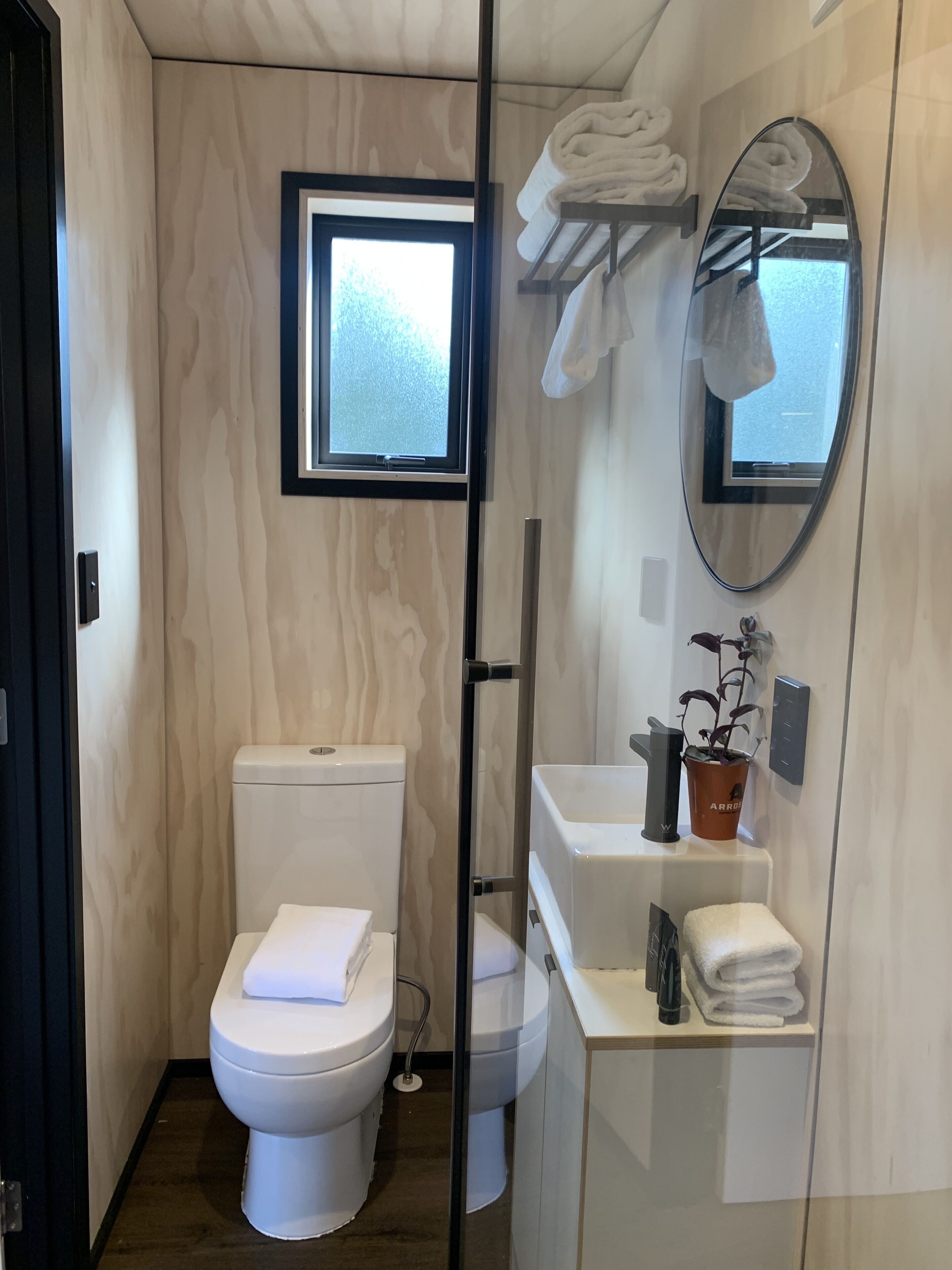 A compact bathroom with a toilet, a sink, a mirror, and a window.
