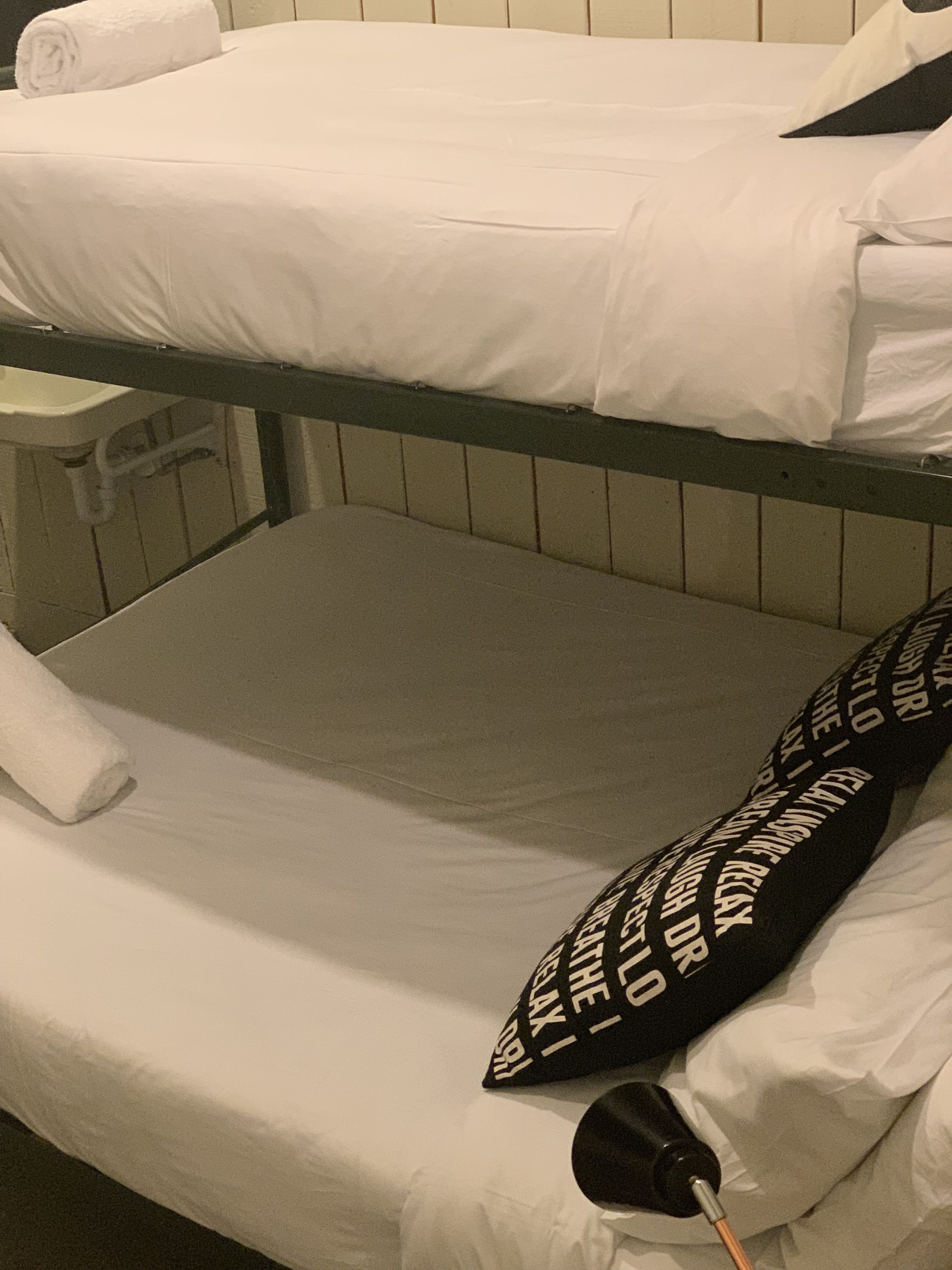 A bunk bed with white bedding and a black pillow with white text.
