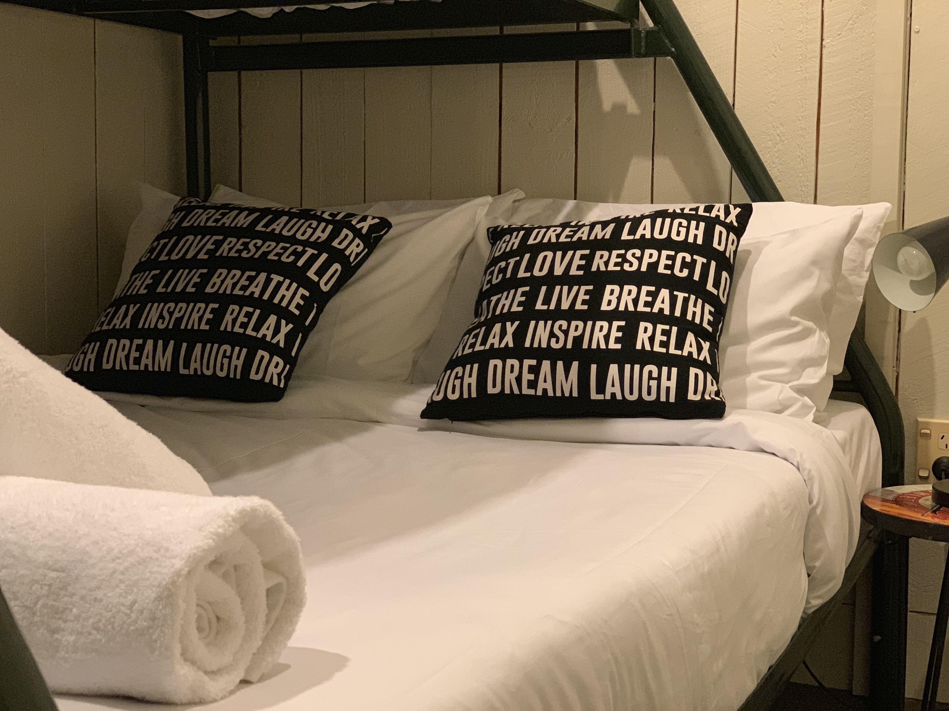 Een stapelbed met witte beddengoed en twee zwarte kussens met witte tekst.