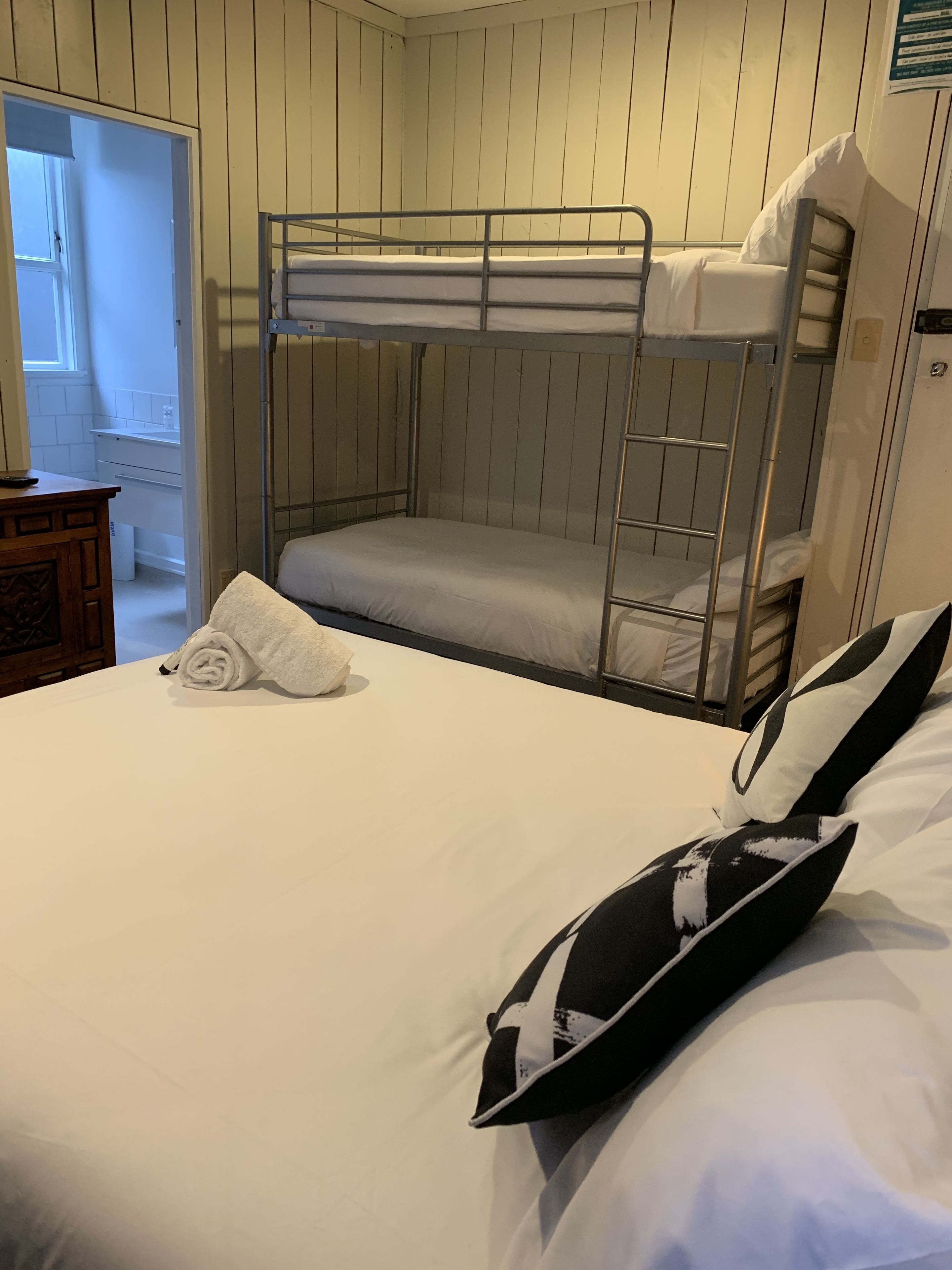 A bunk bed room with a neatly made bed, a rolled towel, and a pillow.