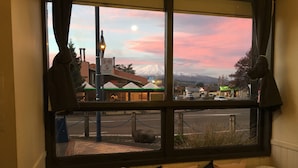 A view from a window with a bench and cushions, overlooking a street with buildings and a mountain in the background. - Snowman Lodge (Ohakune)