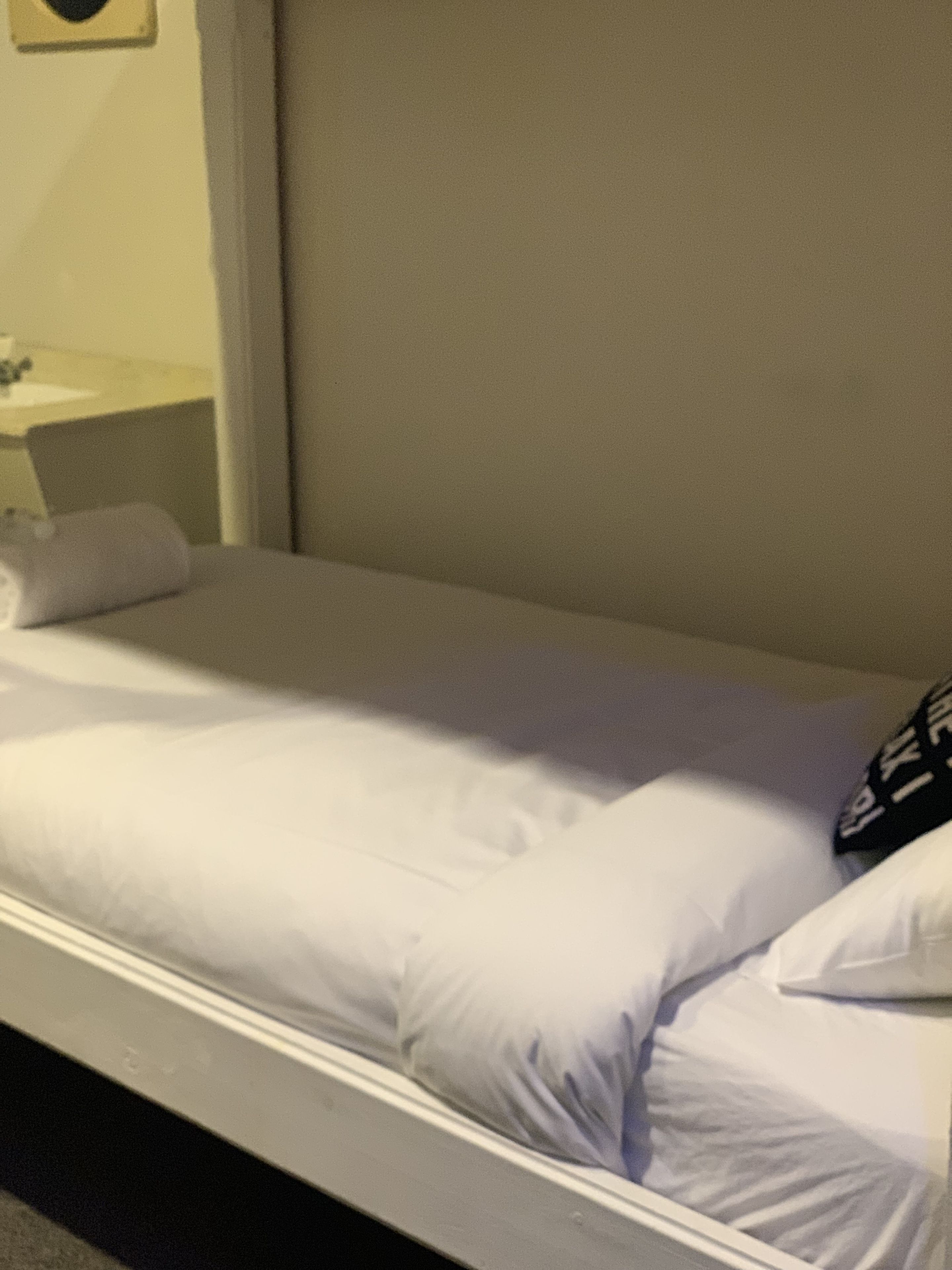 A single bed with white linens in a hotel room.