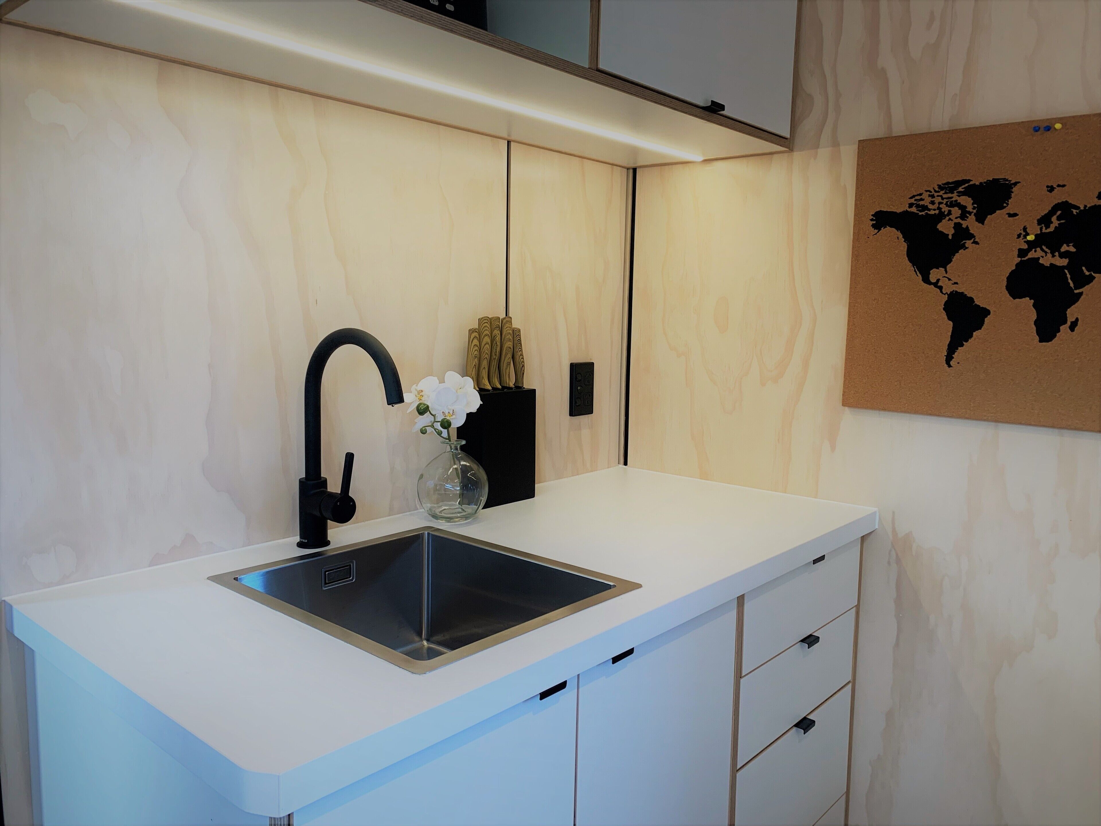 A modern kitchen with a white countertop, black faucet, and a world map on the wall.
