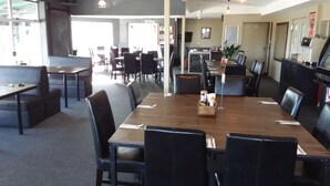 A spacious dining area with a long wooden table, black chairs, and a casual seating area with sofas and tables. - Pine Lake View Lodge (Kaiapoi)