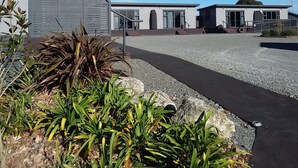 A modern building with a covered outdoor area, a gravel driveway, and some greenery. - Pine Lake View Lodge (Kaiapoi)