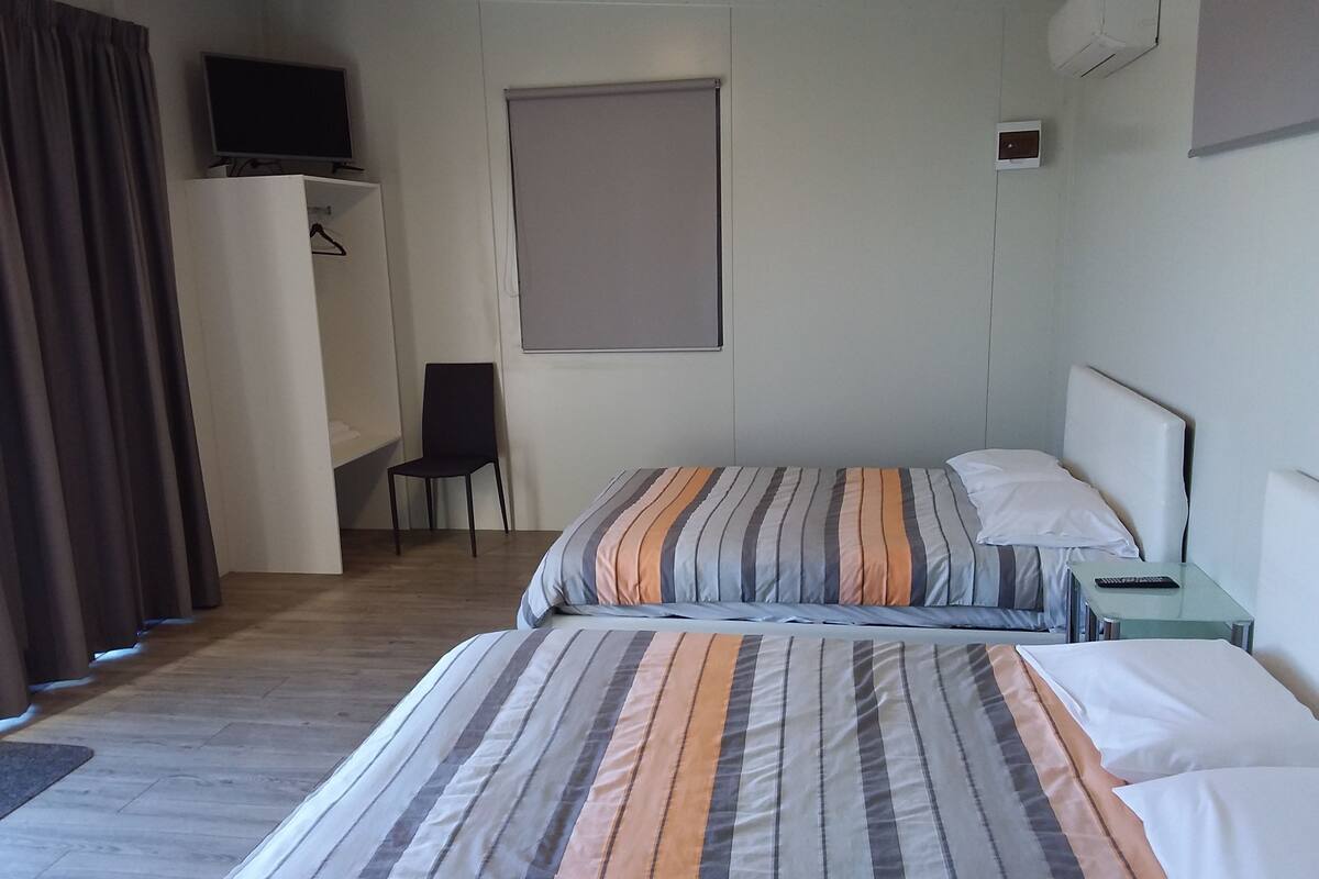 Quarto de hotel com cama, cadeira, escrivaninha, televisão e janela.