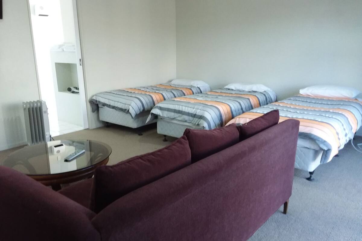 Quarto de hotel com duas camas de solteiro, um sofá, uma mesinha e um radiador.