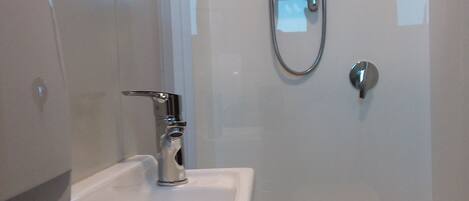 Un baño moderno con cabina de ducha de vidrio, un lavamanos blanco y un grifo de acero inoxidable.