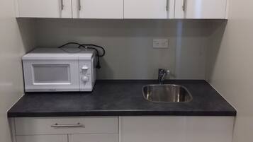 Una kitchenette compacta con microondas, lavamanos y armarios de almacenamiento.