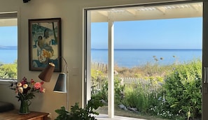 A room with a view of the sea, a painting on the wall, and a lamp. - Beachfront Bach, moments to ocean, breathtaking views, family friendly, Wi-Fi (Patons Rock)