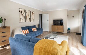 A modern living room with a sofa, a coffee table, and a television. - The Nest in The Wood - peaceful & private, and walking distance to Nelson City (Nelson City)