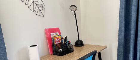 Un espacio de trabajo con un escritorio de madera, una silla de oficina azul, una lámpara blanca y una obra de arte en la pared.