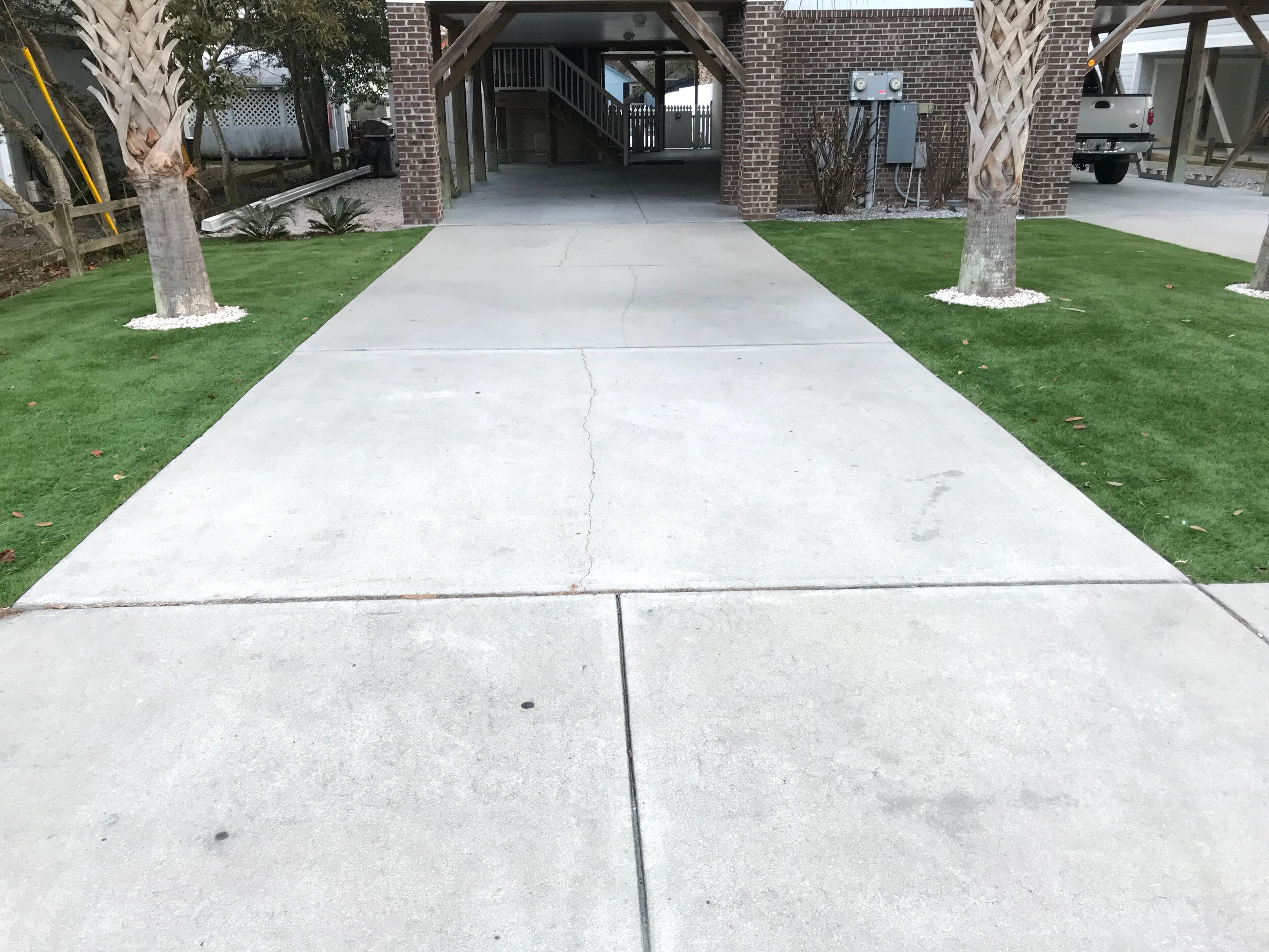 Un chemin en béton menant à l’entrée d’un bâtiment dont la façade est en briques et qui est doté d’un espace abrité.