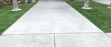 Un chemin en béton menant à l’entrée d’un bâtiment dont la façade est en briques et qui est doté d’un espace abrité.