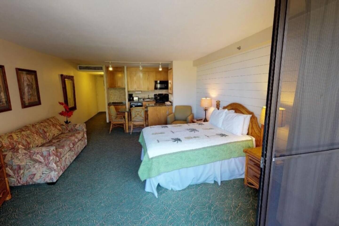 A hotel room with a bed, a sofa, a kitchenette, and a dining area.