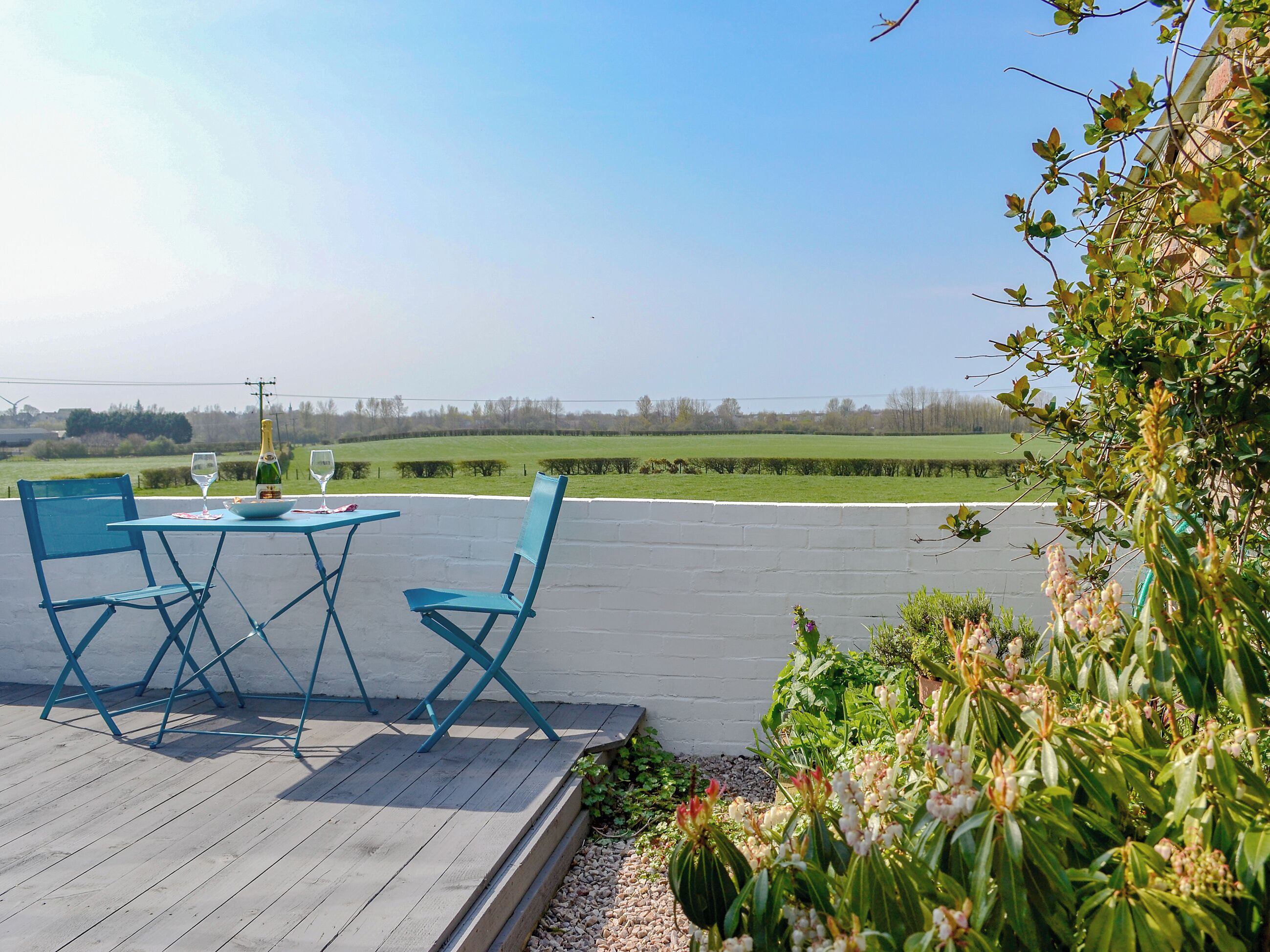 Une terrasse extérieure avec une table et des chaises, une bouteille de champagne et un verre.