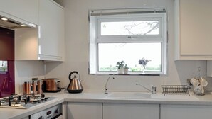 A modern kitchen with white cabinetry, a stainless steel kettle, a toaster, and a sink with a window above it.