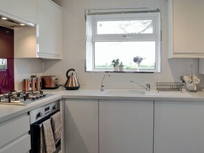 A modern kitchen with white cabinetry, a stainless steel kettle, a toaster, and a sink with a window above it.