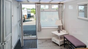 A compact room with a wooden floor, a small white table with a lamp, a bench, and a door leading outside.