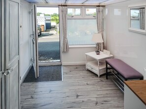 A compact room with a wooden floor, a small white table with a lamp, a bench, and a door leading outside.