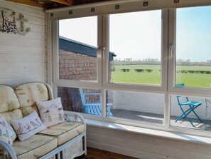 A cozy room with a wicker sofa and cushions, a window with a view of a brick wall and a green field.