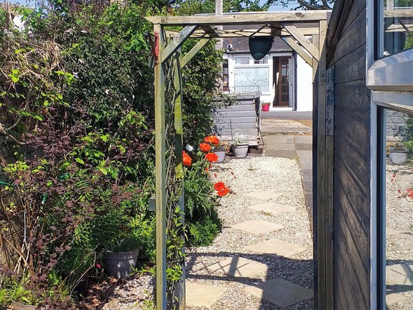 Un sendero de jardín con macetas y una estructura de pérgola de madera.