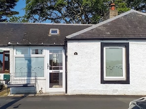 A white building with a black-framed window, a small door, and a bench outside.