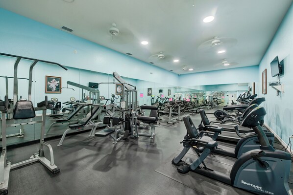 A gym with various exercise equipment, including treadmills and weight machines, and mirrors on the walls.