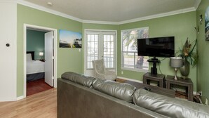 A living room with a leather sofa, a television, and a window with blinds. - Dog-Friendly Beach Retreat with Pool, Hot Tub, and Short Walk to the Beach (Corpus Christi)