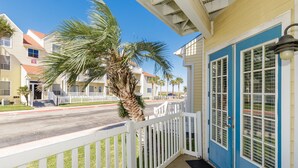 A coastal building with a blue door, white railings, and a palm tree in the foreground. - Dog-Friendly Beach Retreat with Pool, Hot Tub, and Short Walk to the Beach (Corpus Christi)