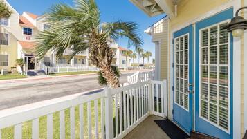 A coastal building with a blue door, white railings, and a palm tree in the foreground.