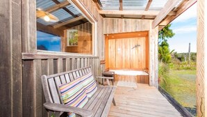 Una terraza de madera con un banco y una pequeña mesa, que conduce a una puerta de madera con un ventanal.