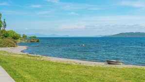 A lakeside view with a boat on the shore, a grassy area, and distant mountains.