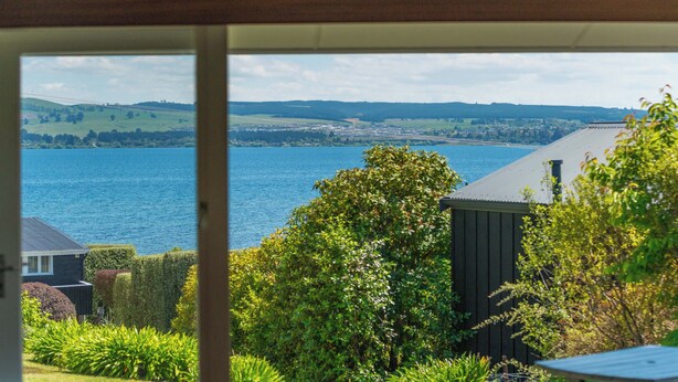 A view from a window overlooking a lake with a house and garden in the foreground.