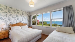 A bedroom with two beds, a wooden headboard, a nightstand, and a window with a view of the sea.