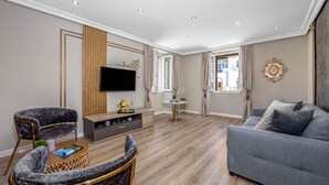 Ein modernes Wohnzimmer mit grauem Sofa, zwei Sesseln, einem Holztisch und einem flachbildfernseher an der Wand.