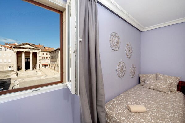 Une chambre avec un lit, une fenêtre avec des rideaux et une vue sur un bâtiment à colonnes.