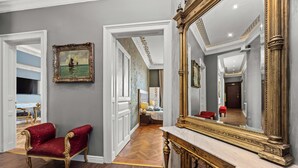 Un'imponente sala con una poltrona in velluto rosso, un ampio specchio decorato e un quadro appeso al muro.