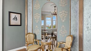 Una stanza con due poltrone decorate, un tavolino con una bottiglia e bicchieri, e un quadro appeso al muro.
